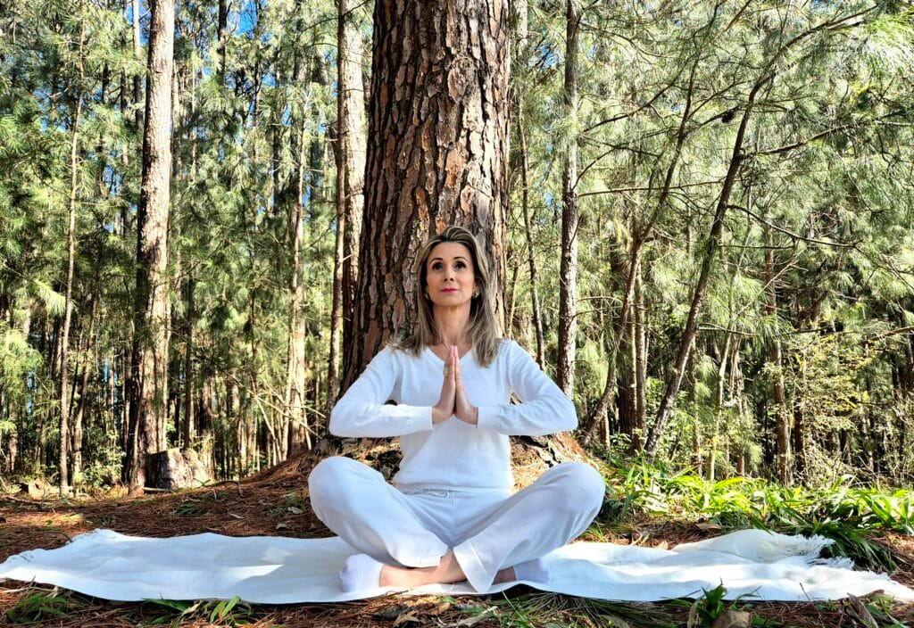 A woman sitting in the middle of a forest doing yoga